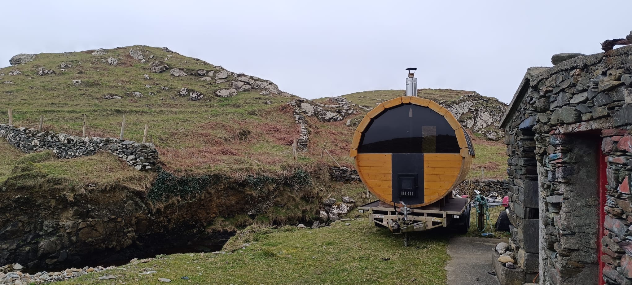 The barrel sauna against an old stone wall and Mayo hillside