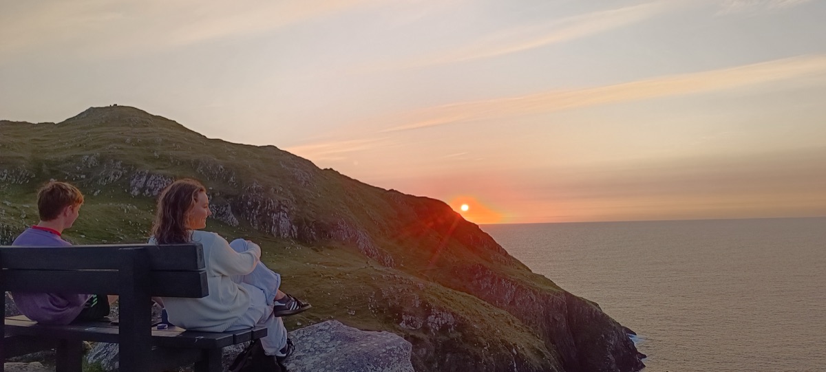 Two people on a bench watching the sun set behind the cliff walk