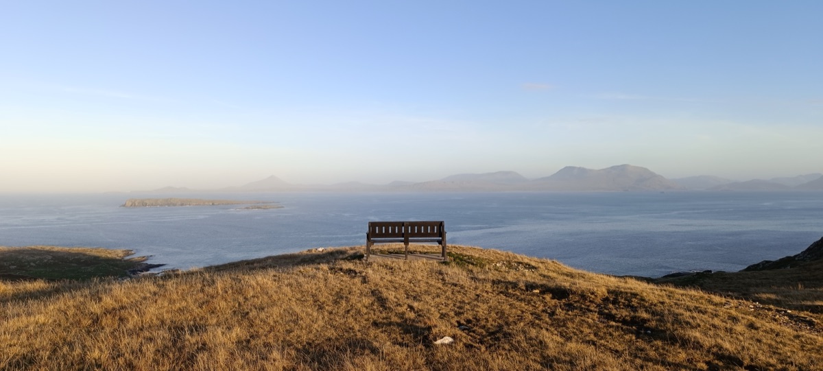 A solitary bench on golden grass overlooking the Atlantic and the Mayo mountains