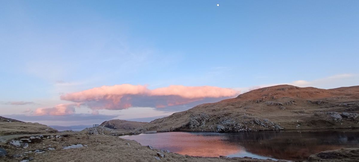 Pink cloud reflected in a still hill lake at dusk, moon rising