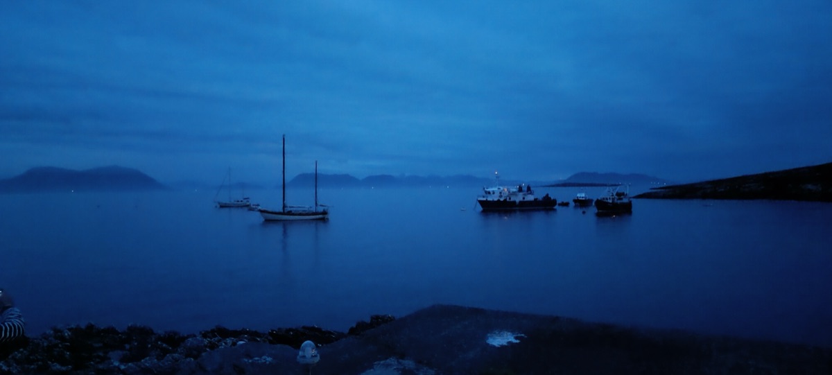 Sailboat and fishing boats anchored in the harbour at blue hour, mountains in mist